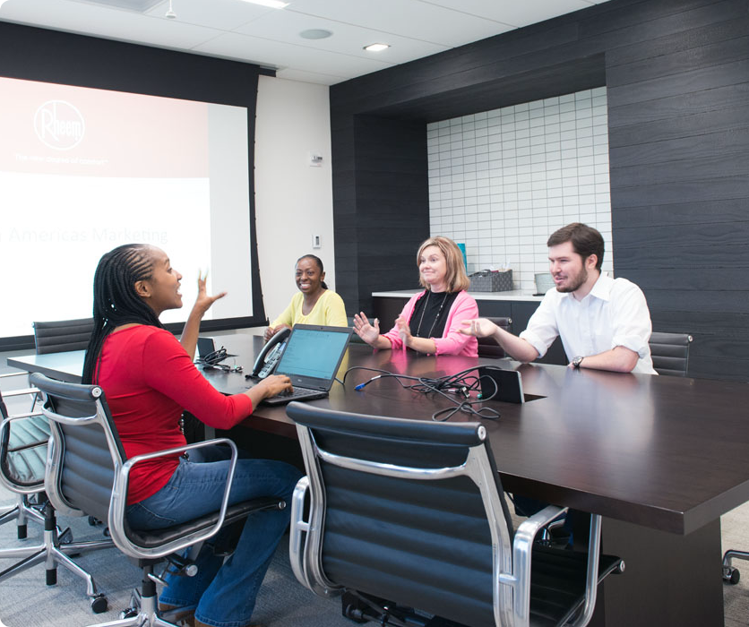 A diverse group of four people at a desk in a conference room smiling at Rheem